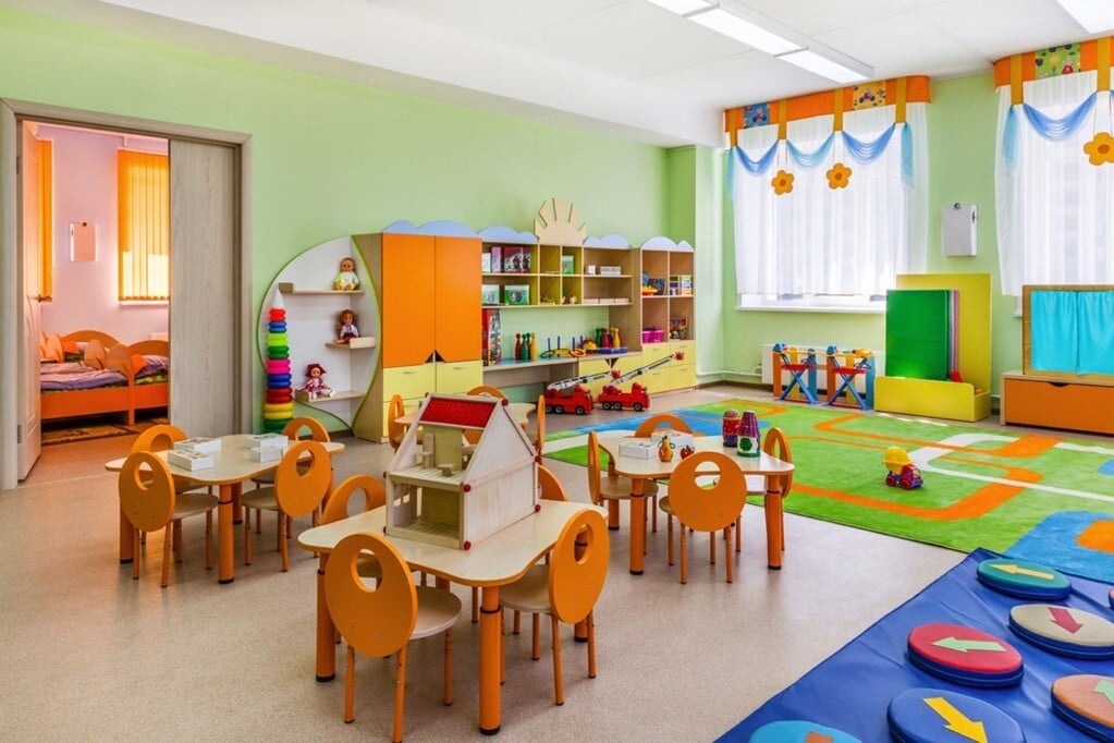 colorful preschool classroom with small tables and chairs and a bookshelf