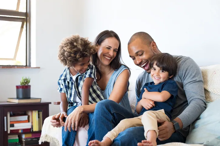 A mother, father, and their two young children laughing together on the couch at home